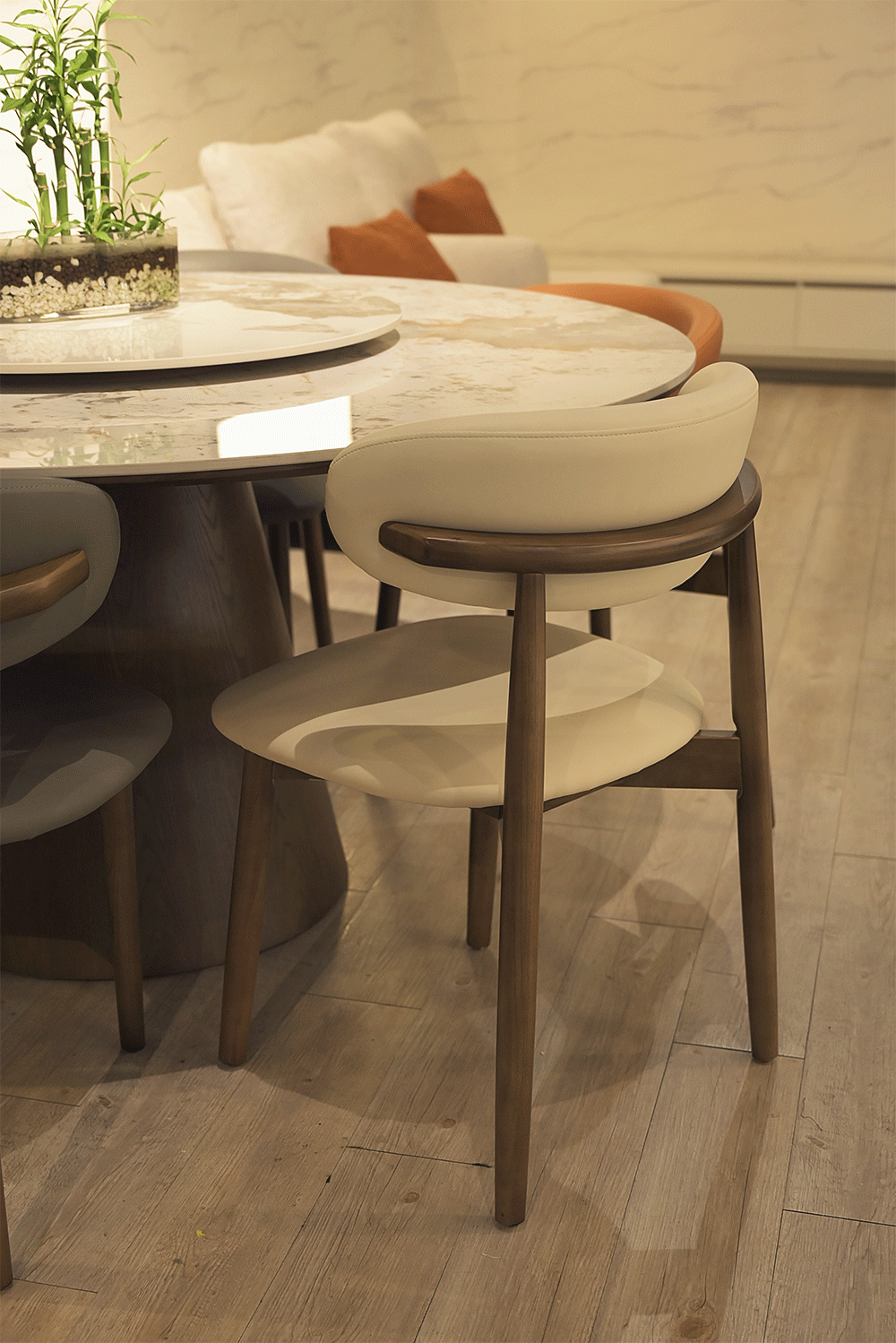 Modern dining chair with wooden legs and cream cushion near marble table.